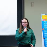 Female college student with a microphone presenting on a poster that is on an easel next to her